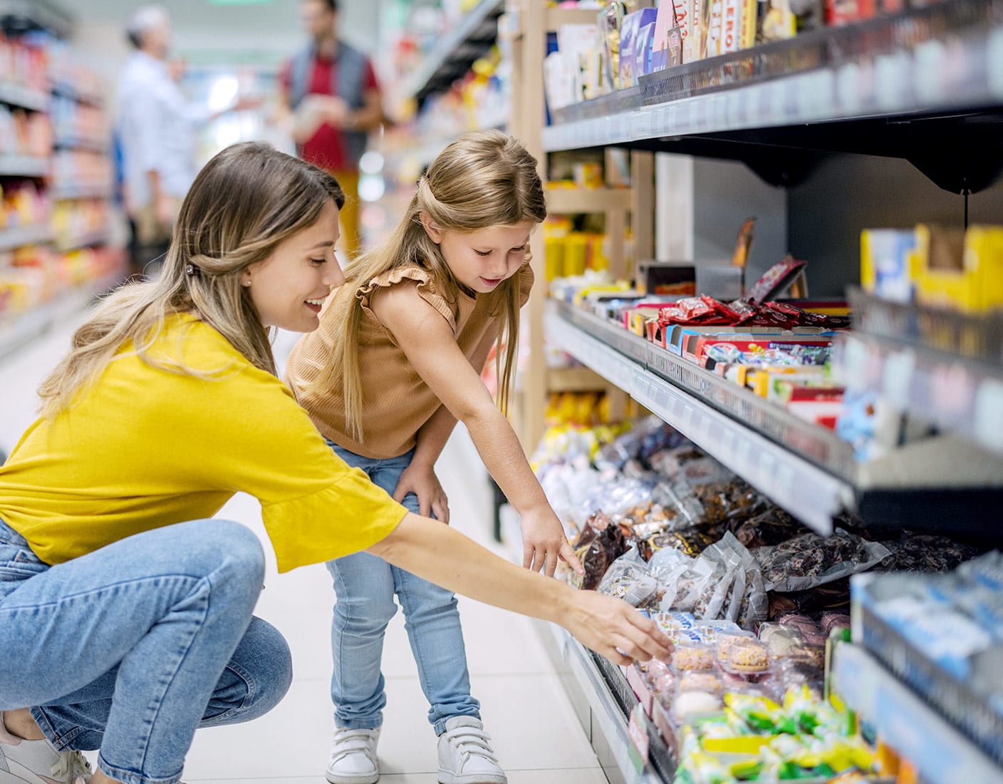 A woman and child examine various food items displayed in a grocery store aisle.